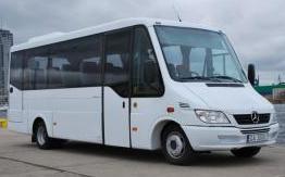 Biały, nowoczesny bus Mercedes-Benz na betonowym podłożu z widokiem na budynki w tle.