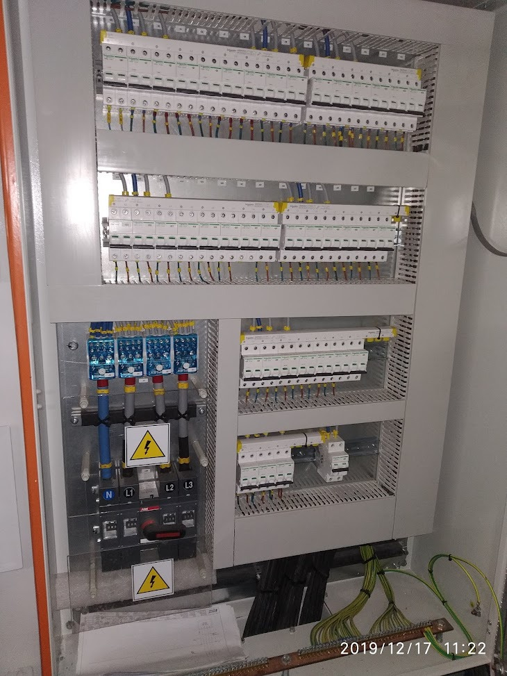 Rozdzielnica elektryczna z zabezpieczeniami nadprądowymi, wyłącznikami różnicowoprądowymi i listwami zaciskowymi, widoczne schematy i oznaczenia faz.