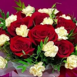 Bujny bukiet czerwonych róż i kremowych goździków z zielonymi listkami na fioletowym tle.