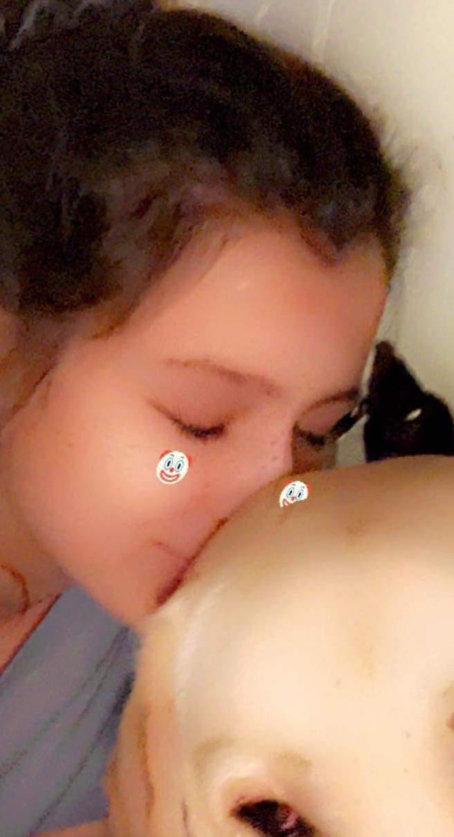 Kobieta z piegami na twarzy delikatnie całuje w głowę niemowlę, oboje mają nałożone filtry z emotikonami klaunów.