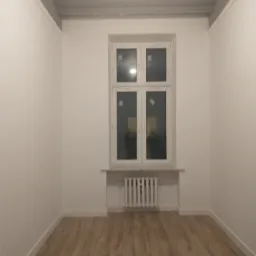 Pusty pokój po remoncie z drewnianą podłogą, białymi ścianami i oknem z grzejnikiem. Widoczna listwa przypodłogowa i sufitowa.