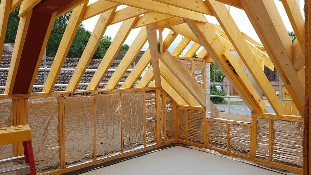 Surowe drewniane krokwie i izolacja folią aluminiową na ścianach poddasza w trakcie adaptacji, widok z wnętrza, drabina na pierwszym planie.