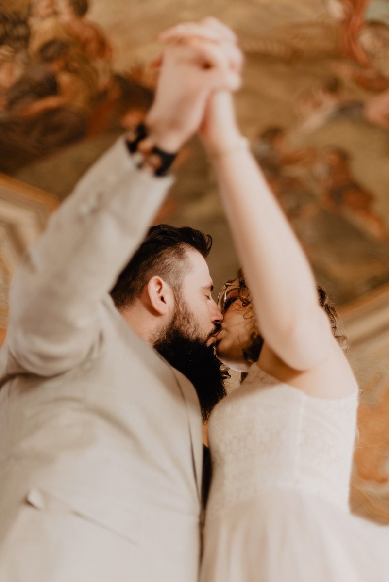 Para młoda całuje się, trzymając się za ręce na tle malowanego sufitu.