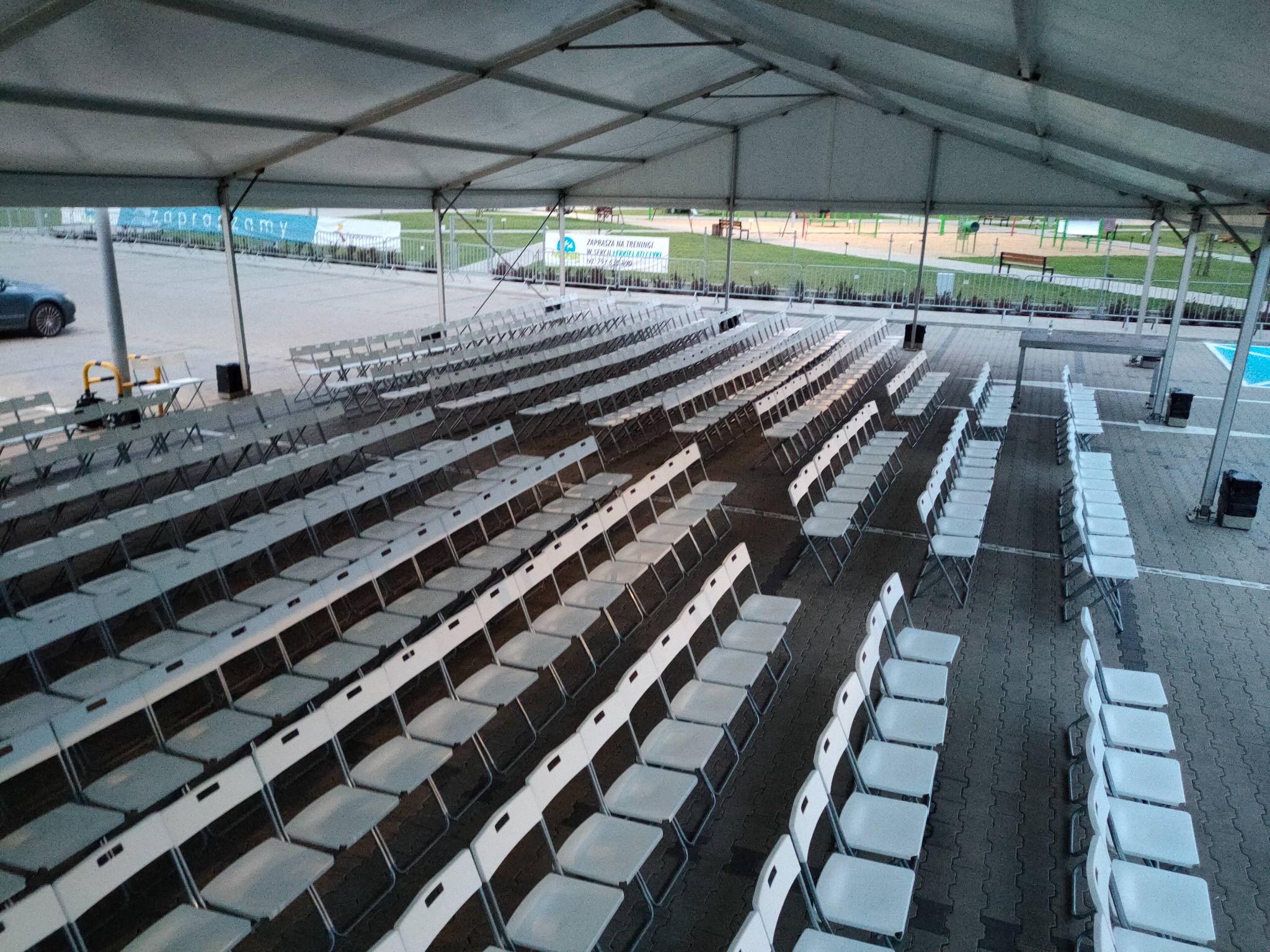 Rzędy białych krzeseł pod dużym, rozłożonym namiotem, widok z góry na przygotowane miejsce wydarzenia.