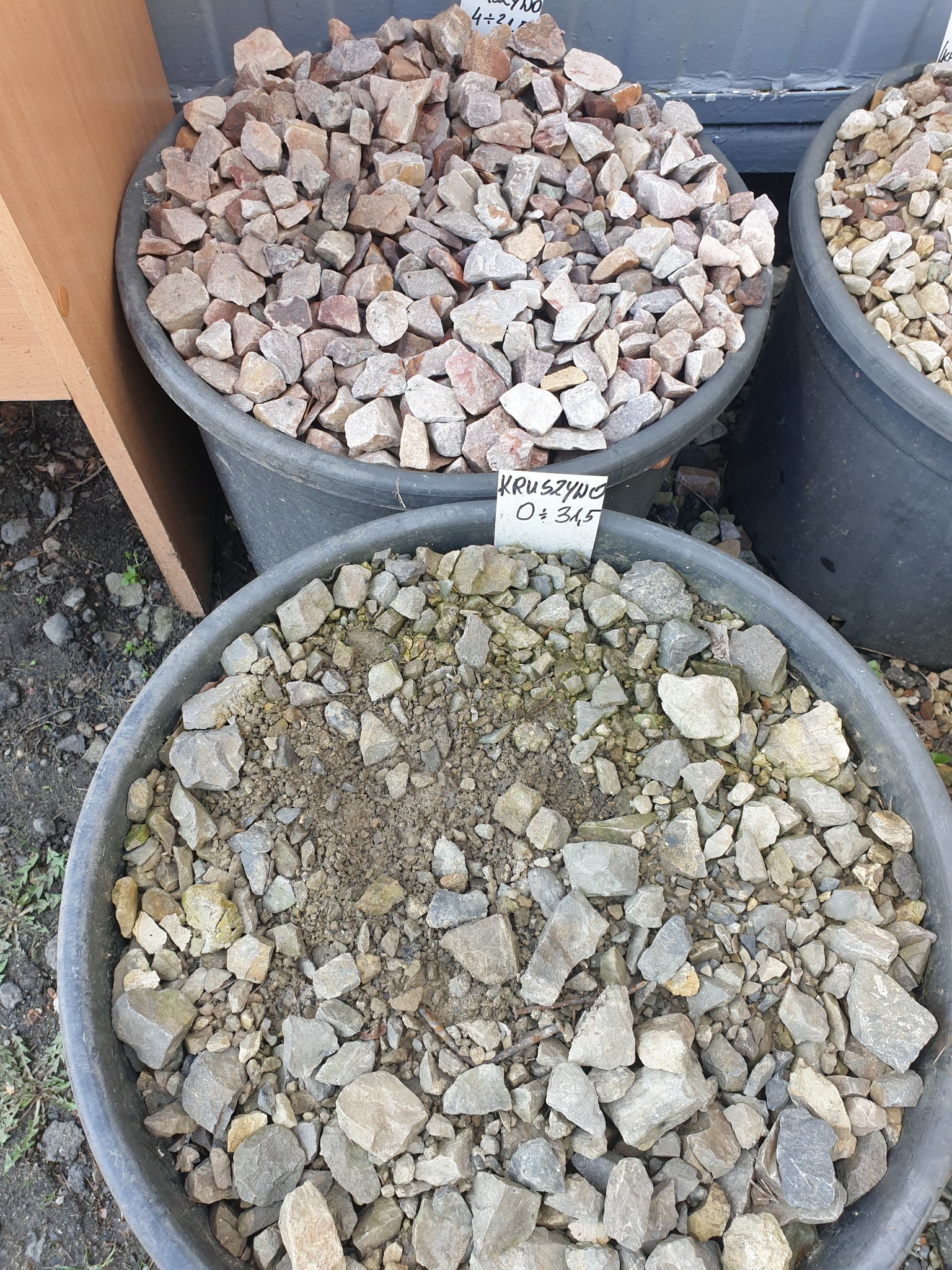 Kruszywo w plastikowych pojemnikach z cenówkami, widoczne różne frakcje i kolory kamieni.