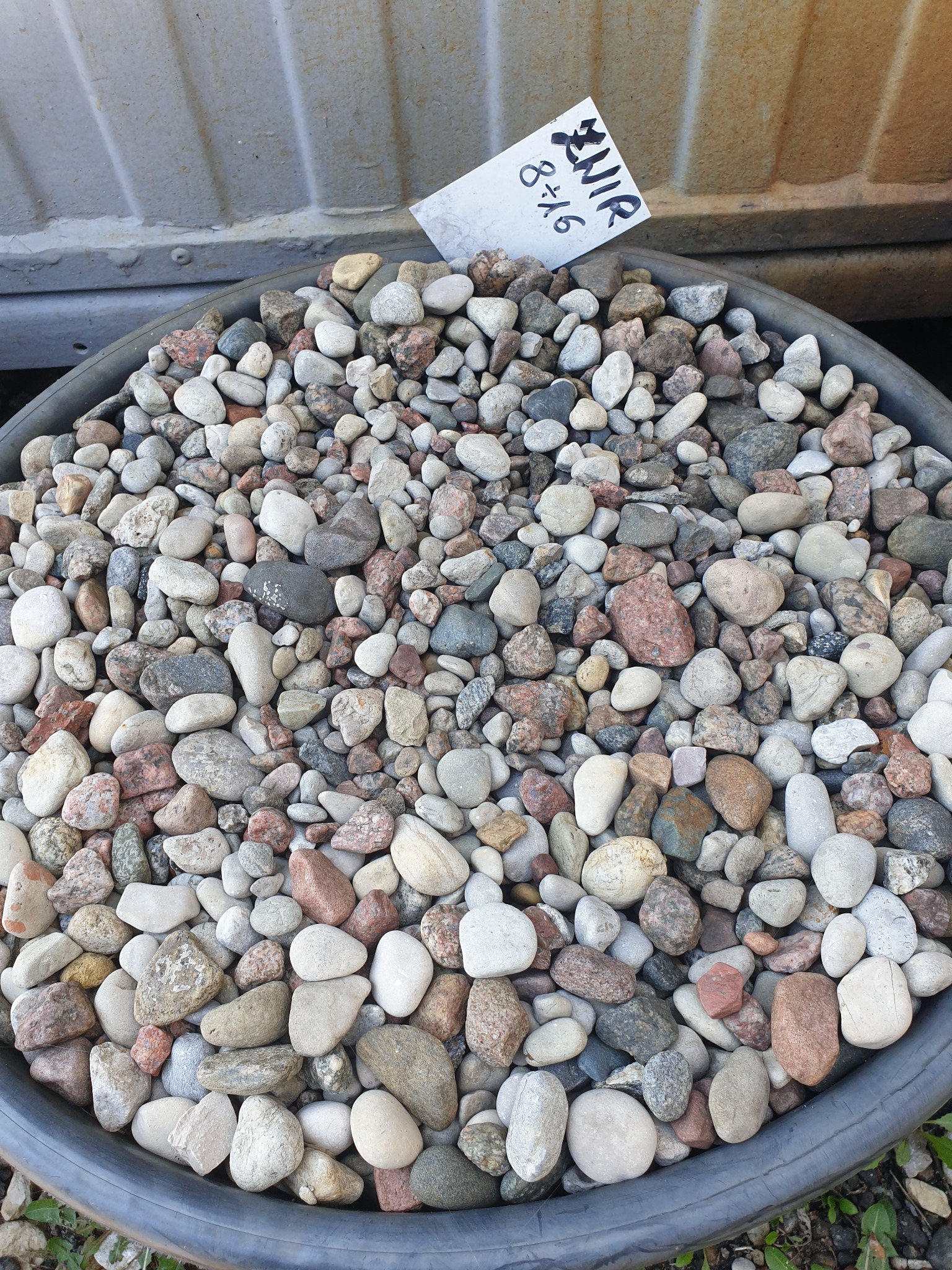 Różnokolorowe otoczaki w szarej misie z kartką z napisem 'Żwir 8x16'.