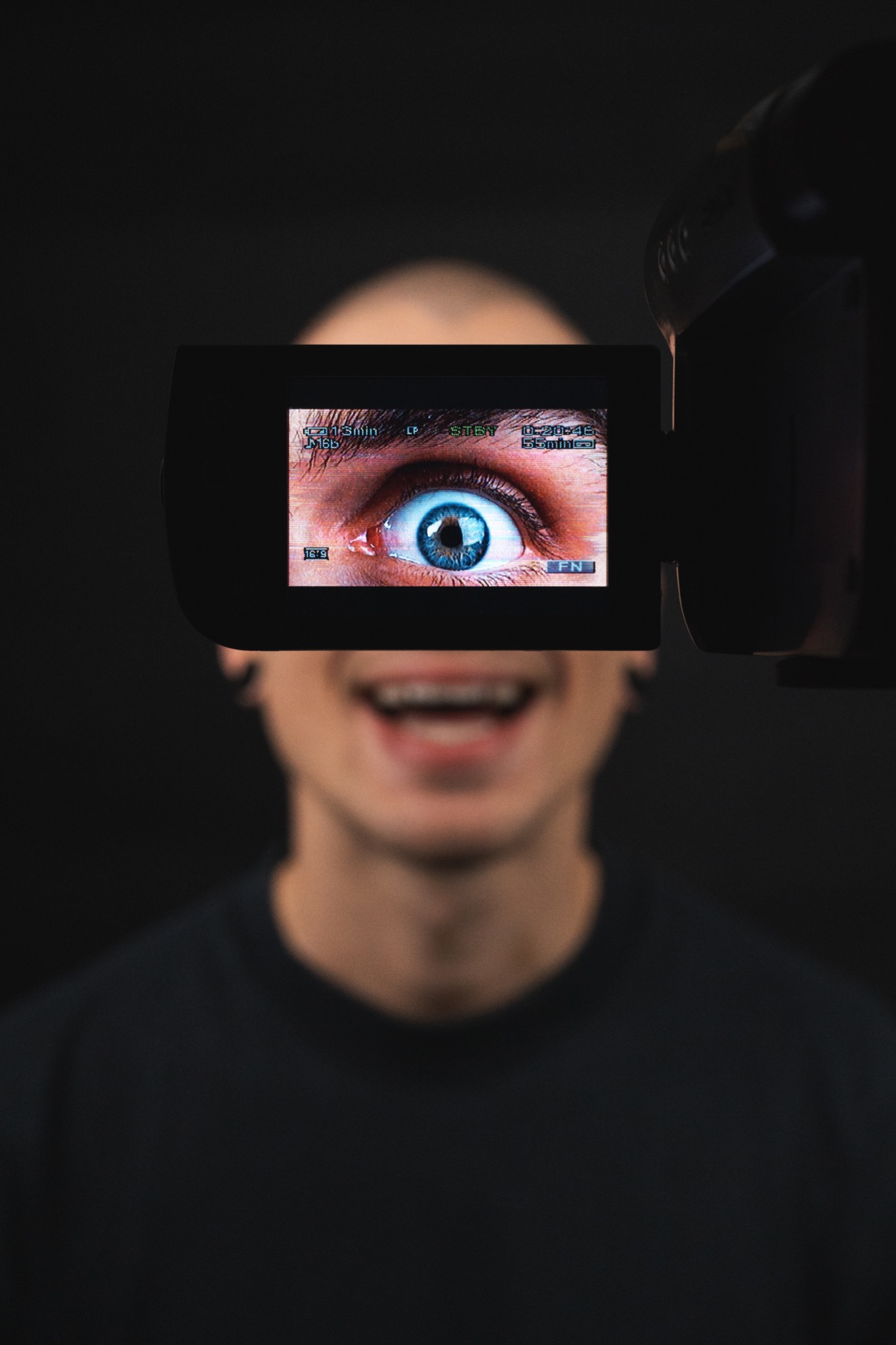 Ekran kamery wideo pokazuje zbliżenie oka, w tle uśmiechnięta, rozmyta twarz osoby.