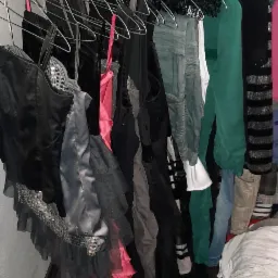 Wieszak z r&oacute;żnorodną odzieżą, w tym sukienki z falbanami i cekinami, widoczny fragment obrazu z motywem miejskim w tle.