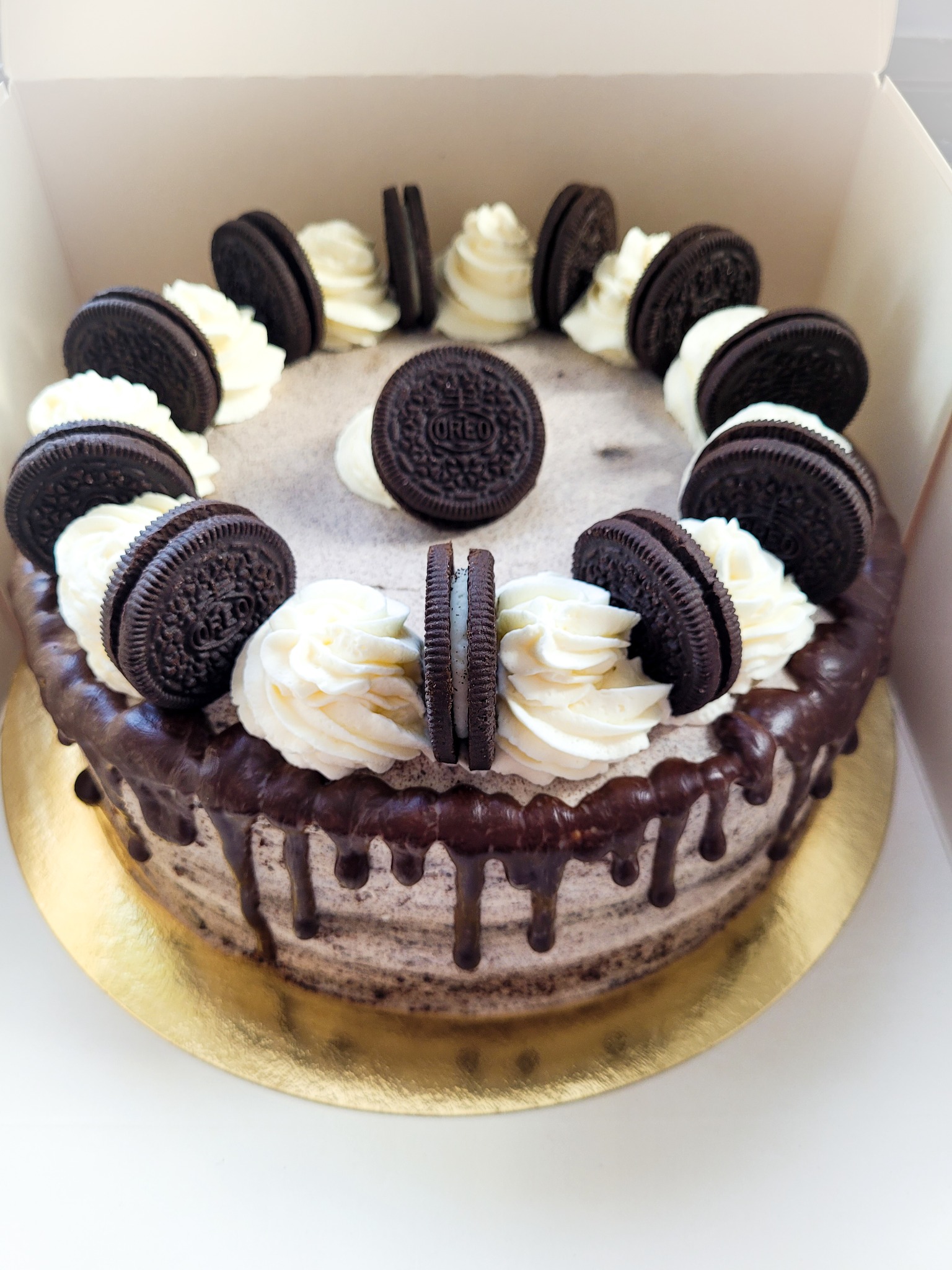 Tort Oreo z kremem śmietankowym i polewą czekoladową, udekorowany ciasteczkami Oreo w pudełku.