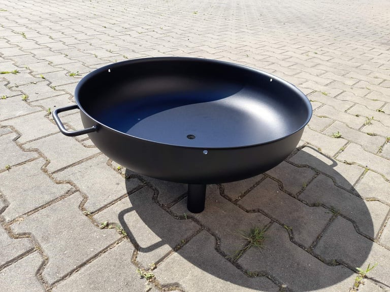 Czarny, metalowy palenisko ogrodowe na trzech nóżkach z uchwytami, stojące na betonowej kostce brukowej w słoneczny dzień.