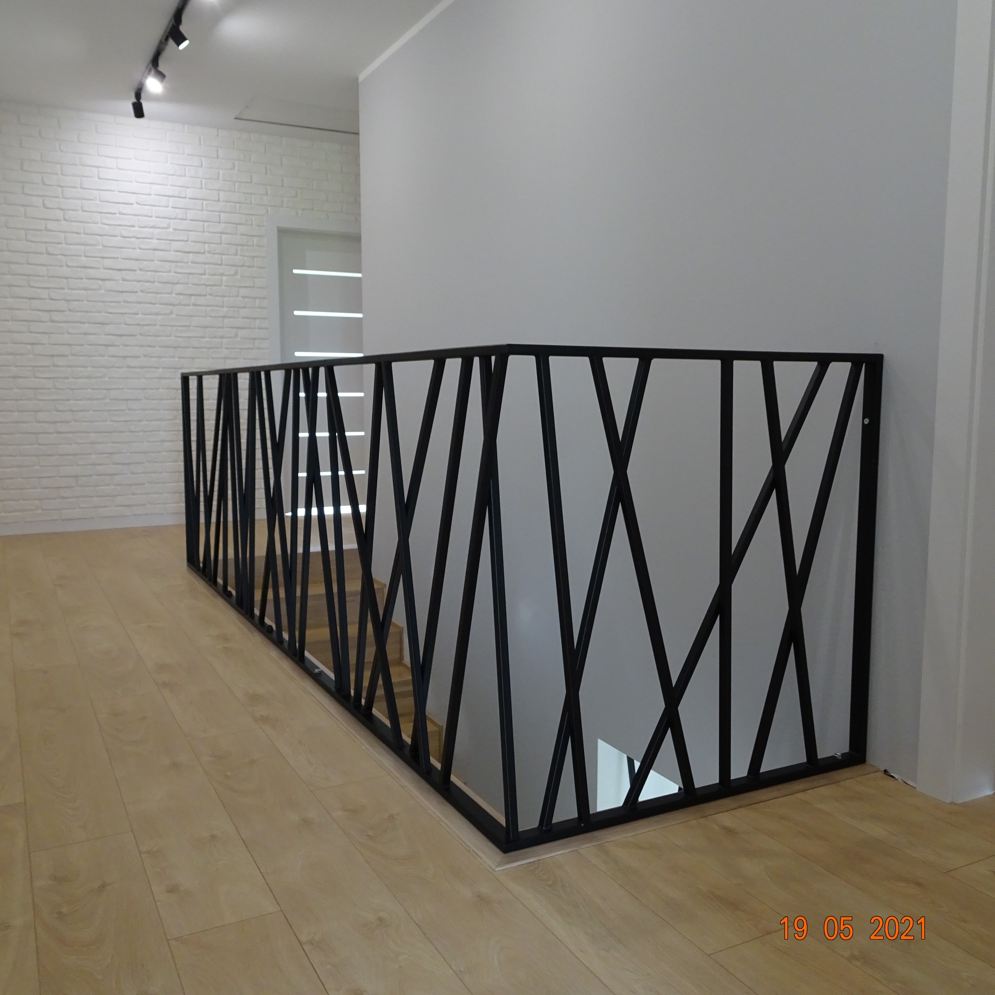 Nowoczesna balustrada schodowa z czarnego metalu o geometrycznym wzorze w Krakowie, widoczna z perspektywy podłogi, z białymi ścianami w tle.