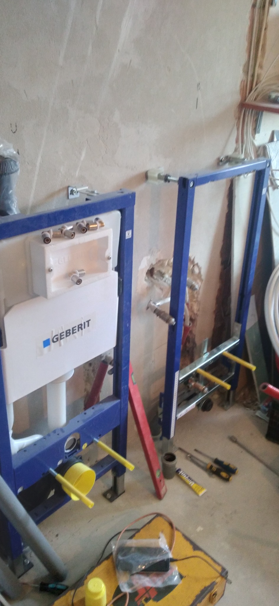 Stelaże podtynkowe Geberit zamontowane przy surowej ścianie, widoczne narzędzia i poziomica, instalacja w trakcie wykonywania.