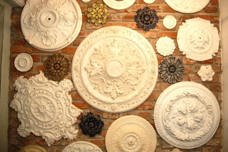 Dekoracyjne rozety sufitowe z gipsu, o zróżnicowanych wzorach i rozmiarach, zamontowane na ścianie z czerwonej cegły.