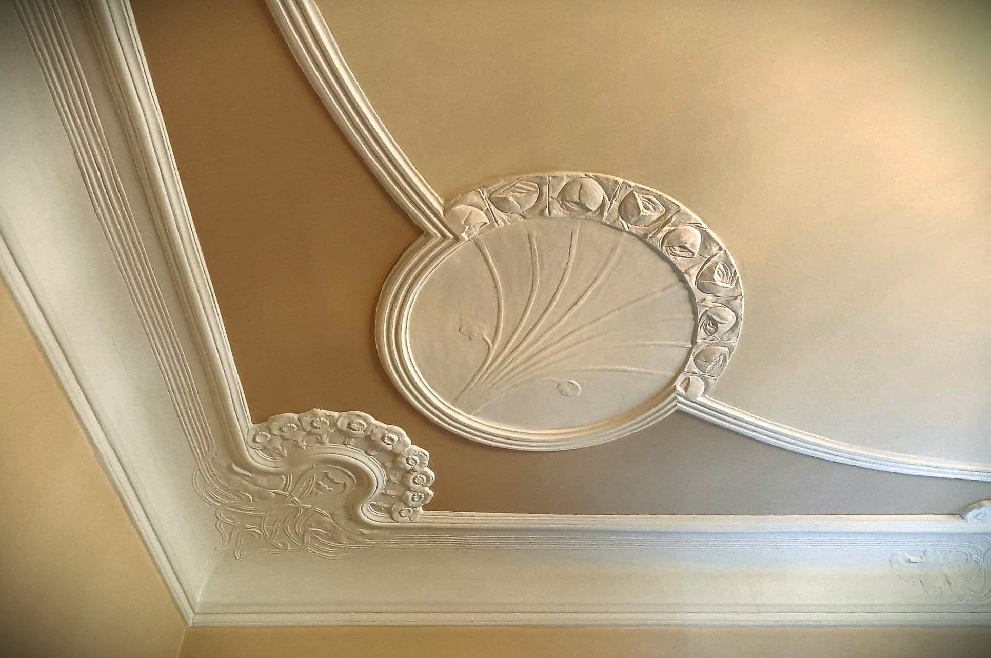 Dekoracyjny sufit z gipsowymi zdobieniami: okrągła rozeta z motywem roślinnym i ornamenty w stylu secesyjnym.