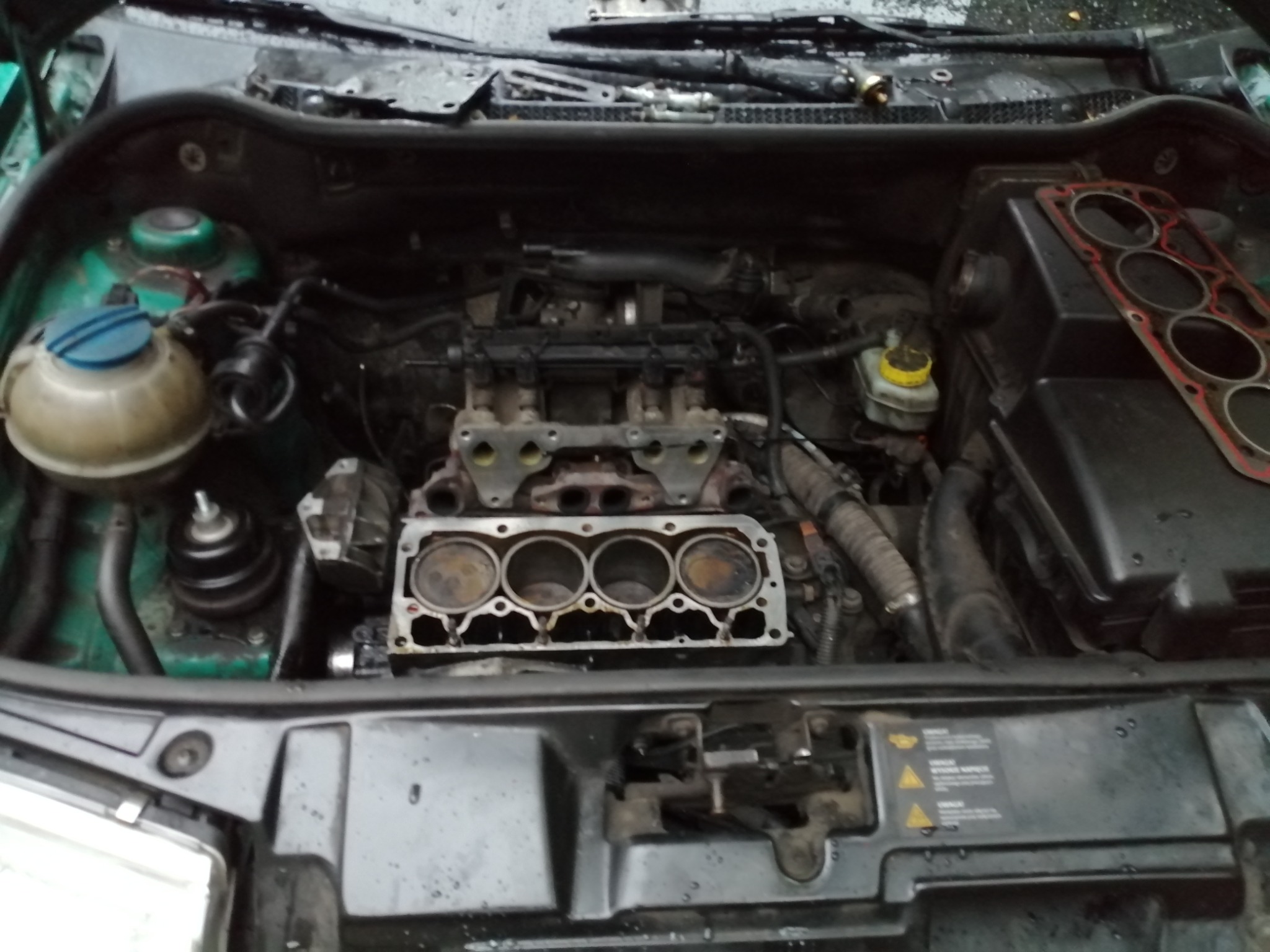 Otwarty silnik samochodowy z widocznym blokiem cylindrów i uszczelką głowicy obok, w trakcie naprawy lub przeglądu.