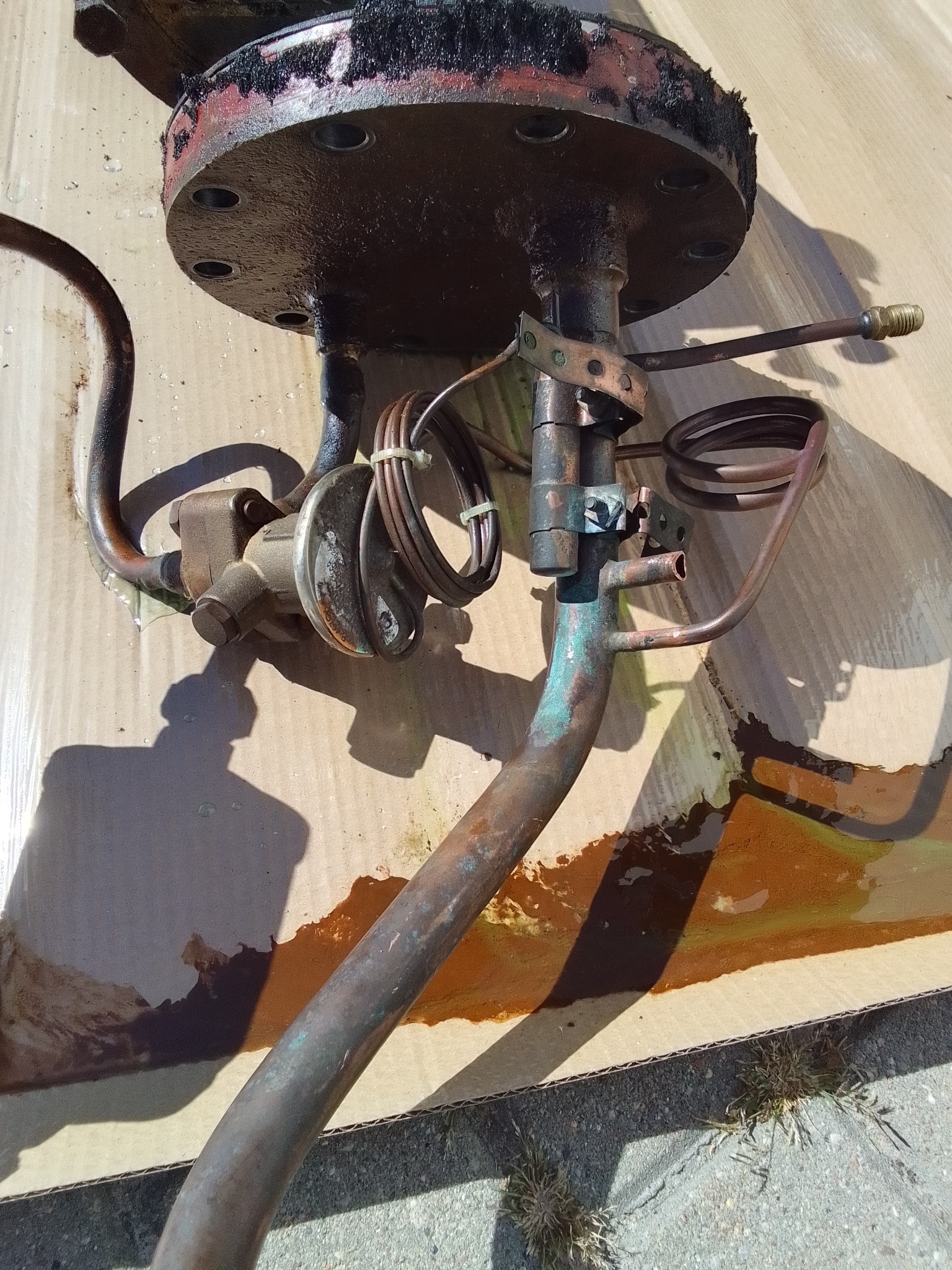 Zdemontowany, skorodowany element instalacji chłodniczej z widocznymi śladami oleju na kartonowym podłożu.