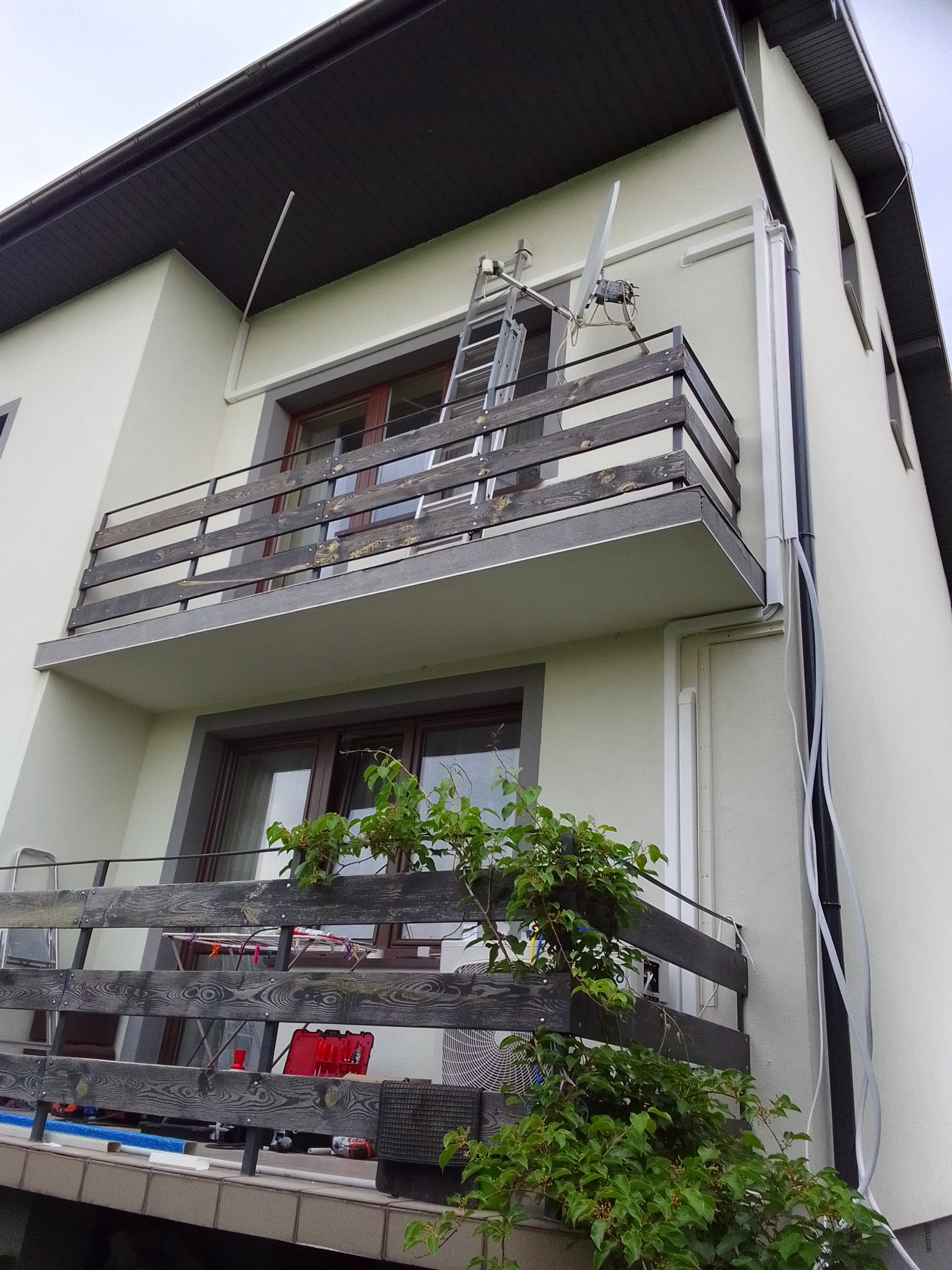 Montaż klimatyzacji na balkonie budynku mieszkalnego, widoczna drabina oparta o balkon, jednostka zewnętrzna klimatyzacji na balkonie, przewody prowadzone po elewacji budynku.