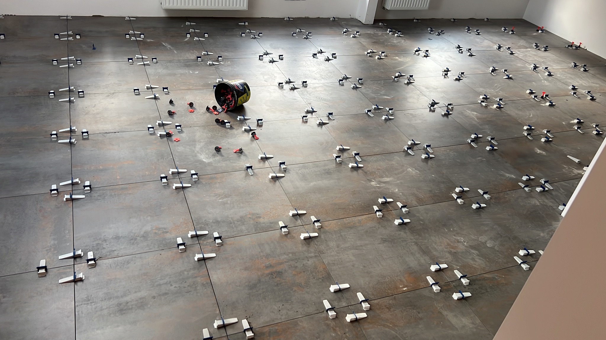 Układanie płytek podłogowych z użyciem systemu poziomowania płytek w Felinowie. Widoczny kubeł z narzędziami glazurniczymi.