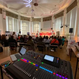 Konsoleta mikserska z laptopem na pierwszym planie, w tle sala konferencyjna z uczestnikami Forum Kobiet i sceną z nagłośnieniem i oświetleniem.