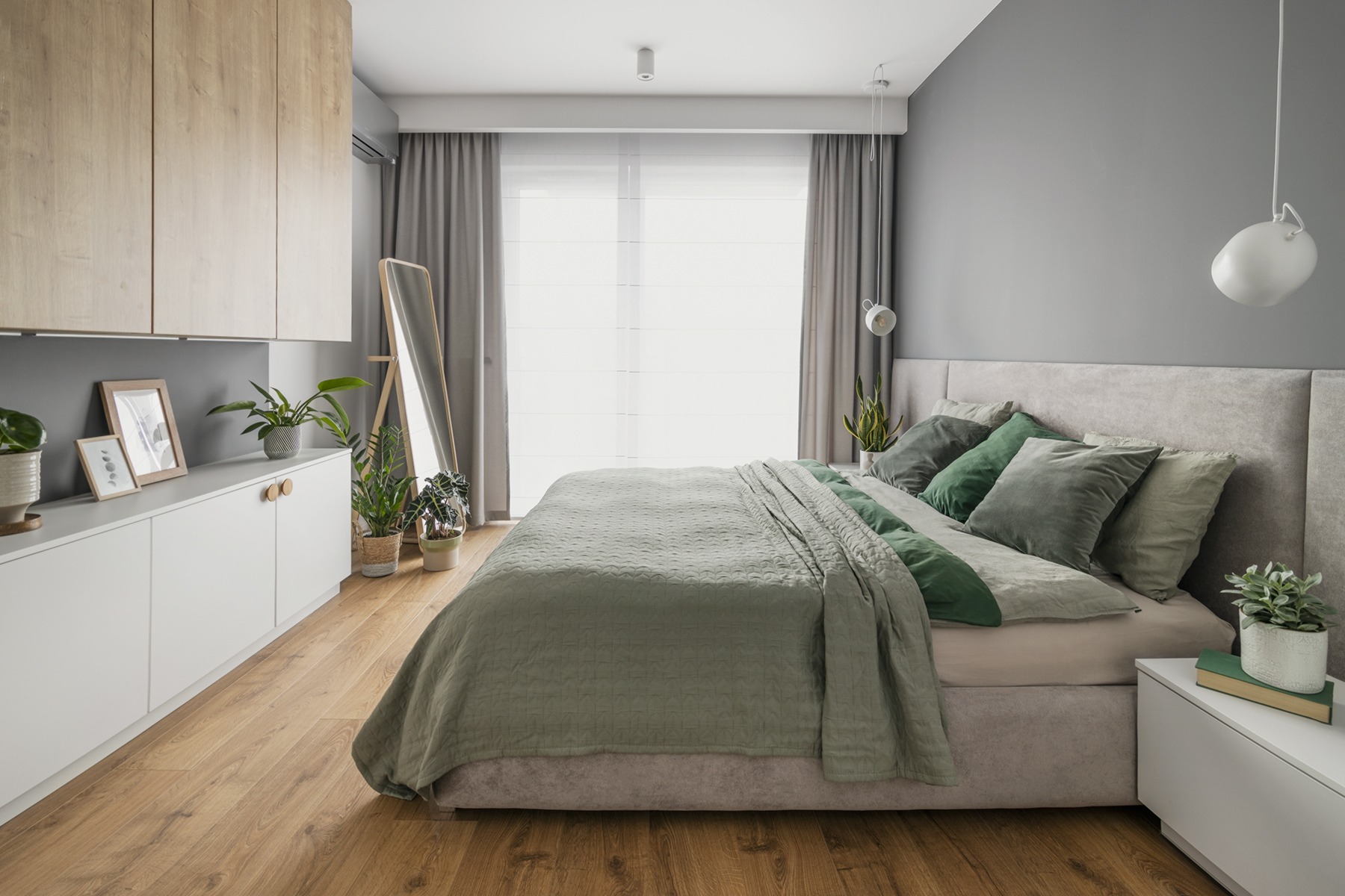 Nowoczesna sypialnia w odcieniach szarości i zieleni z drewnianą podłogą, zabudową meblową i dużym lustrem stojącym.