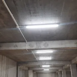 Wnętrze surowego, betonowego garażu podziemnego z zamontowanymi liniami świetlnymi LED i instalacją elektryczną w białych rurkach PCV.