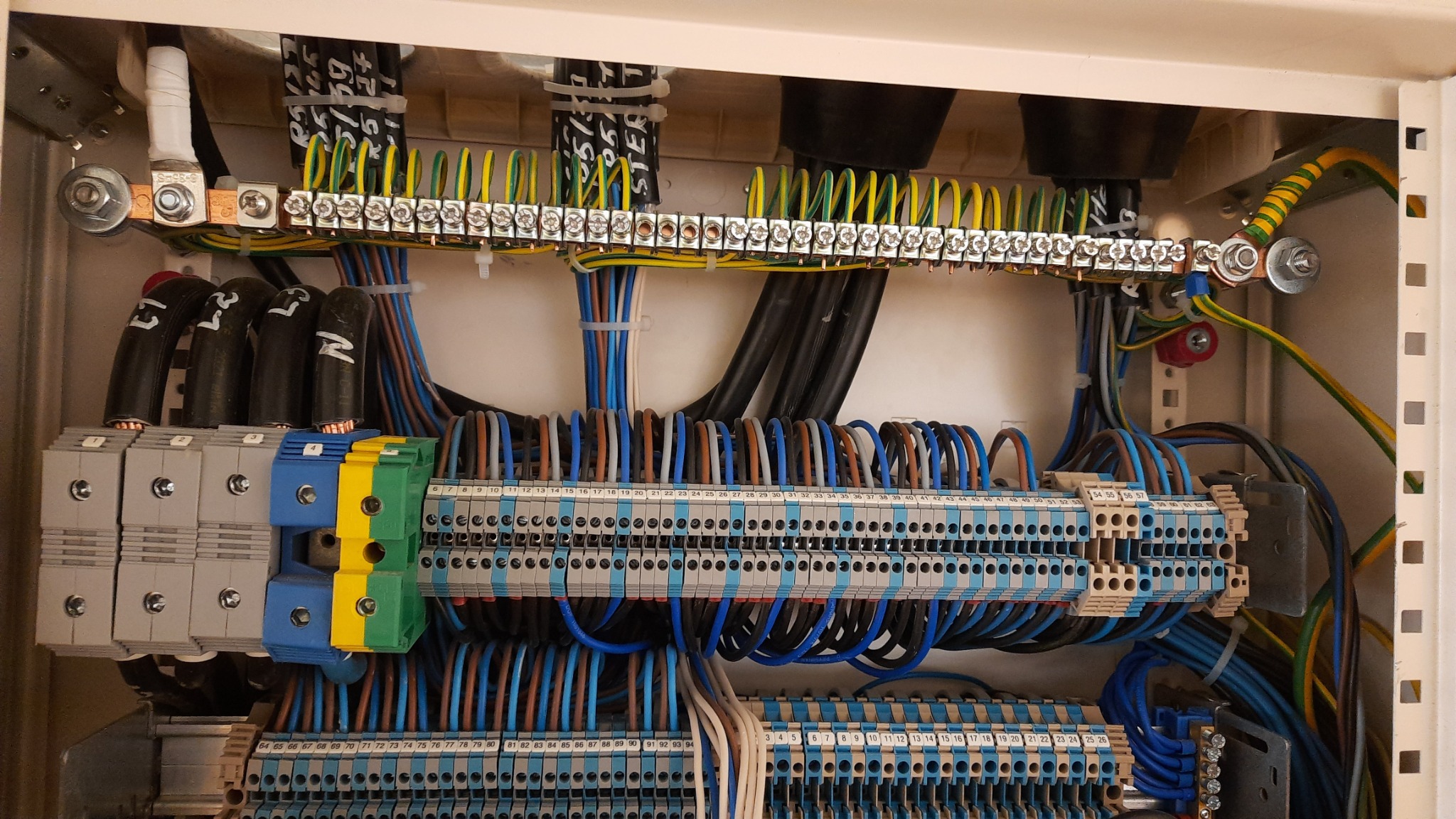 Wnętrze skrzynki elektrycznej z widocznymi listwami zaciskowymi, przewodami o różnych kolorach i grubościach, oraz elementami montażowymi. Zwraca uwagę staranne ułożenie przewodów i ich podłączenie...