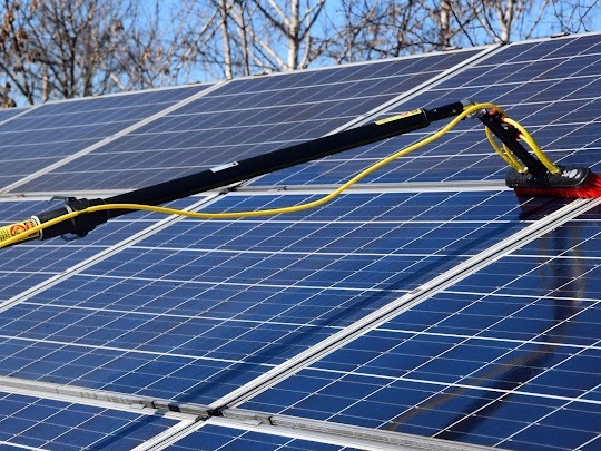 Czyszczenie paneli słonecznych na dachu za pomocą szczotki na teleskopowym wysięgniku z doprowadzeniem wody.