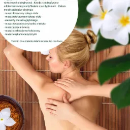 Kobieta podczas masażu ramion w salonie spa, z widoczną misą z kwiatem frangipani, bambusowa mata pod spodem, ulotka reklamowa z ofertą masażu w tle.
