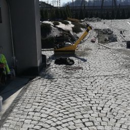 Mariusz Urbanski - Układanie kostki granitowej na podjeździe z użyciem zagęszczarki, widoczne narzędzia i częściowo ułożona nawierzchnia w promieniście ułożonym wzorze.