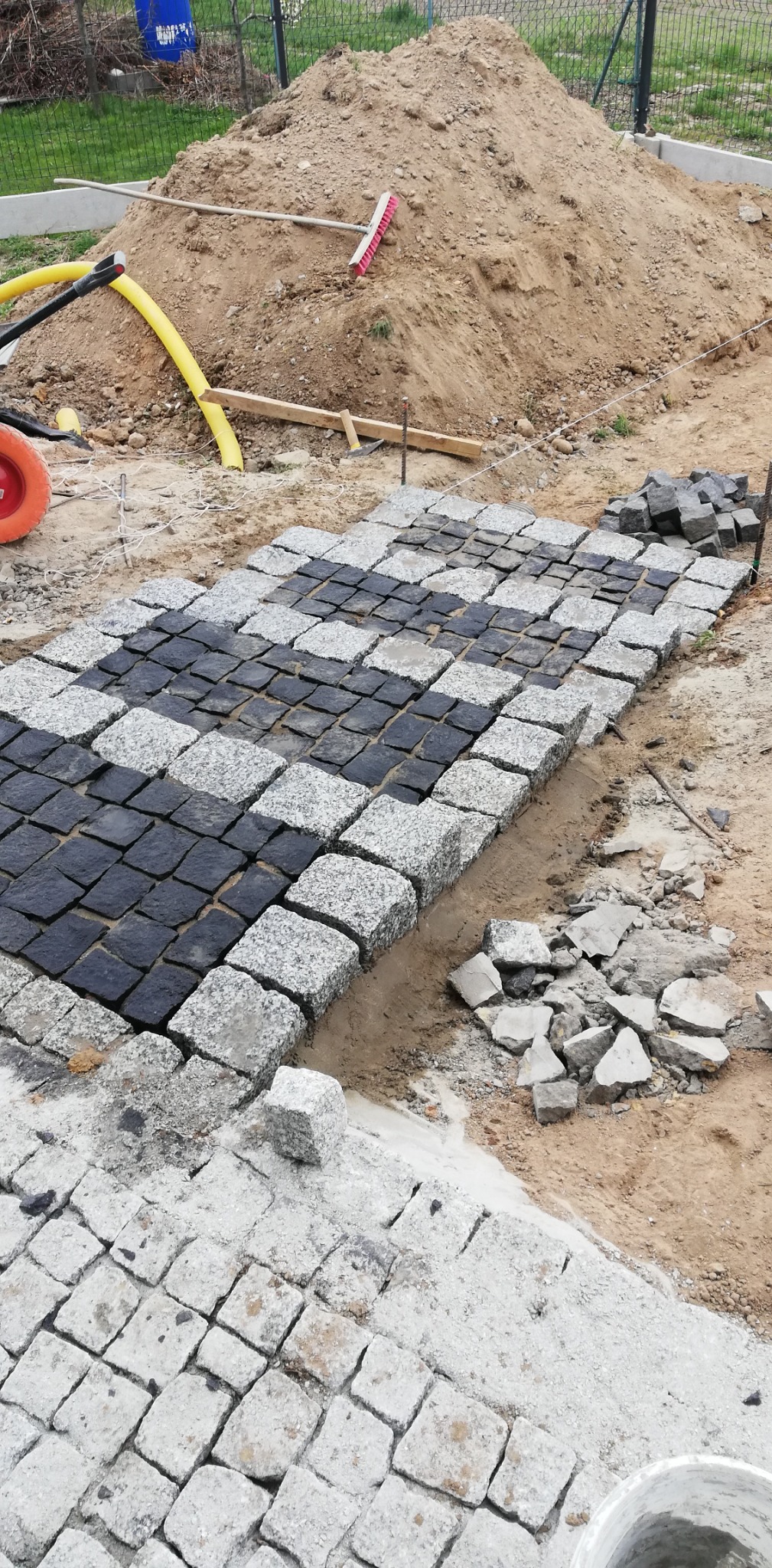 Fragment układanej ścieżki z czarno-szarej kostki granitowej w Świdnicy, widoczny stos kostki, przygotowane podłoże i narzędzia.