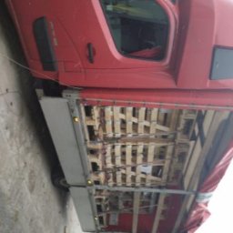 S-trans - Czerwony samochód dostawczy z otwartą przestrzenią ładunkową wypełnioną drewnianymi elementami konstrukcyjnymi, widoczne koła i fragment kabiny.