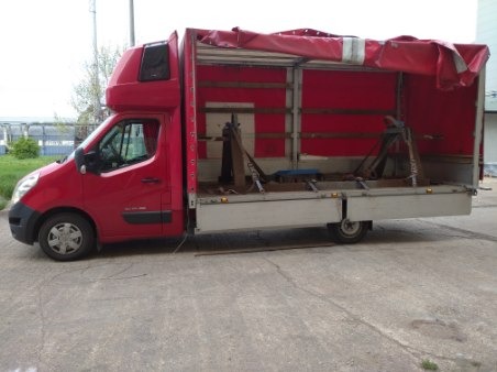 Czerwony samochód dostawczy z otwartą przestrzenią ładunkową, wewnątrz widoczne metalowe konstrukcje zabezpieczone pasami.