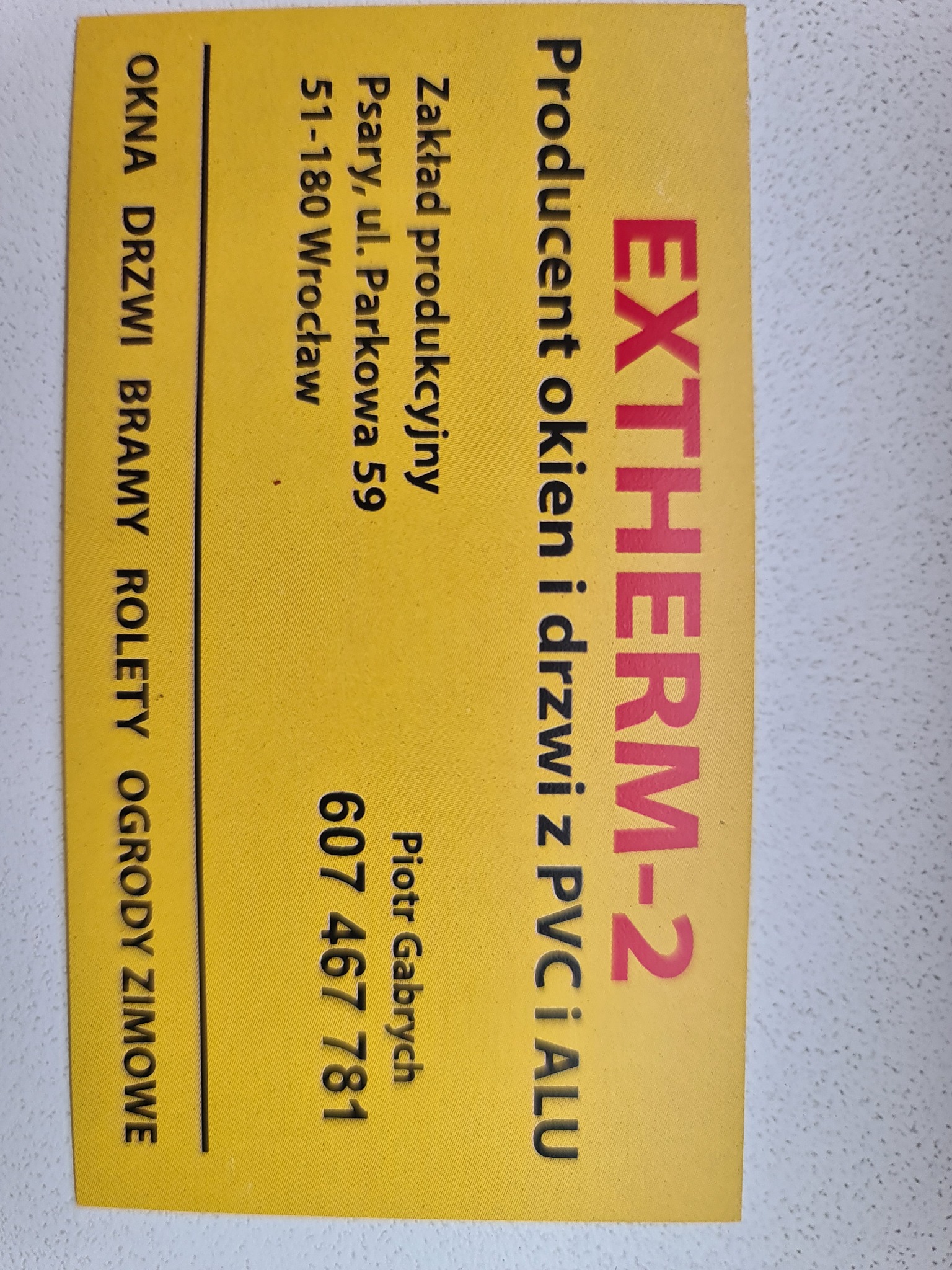 Żółta wizytówka firmy EXTHERM-2, producenta okien i drzwi z PVC i aluminium, z adresem w Psarach i numerem telefonu Piotra Gabrycha, oferującej okna, drzwi, bramy, rolety i ogrody zimowe.