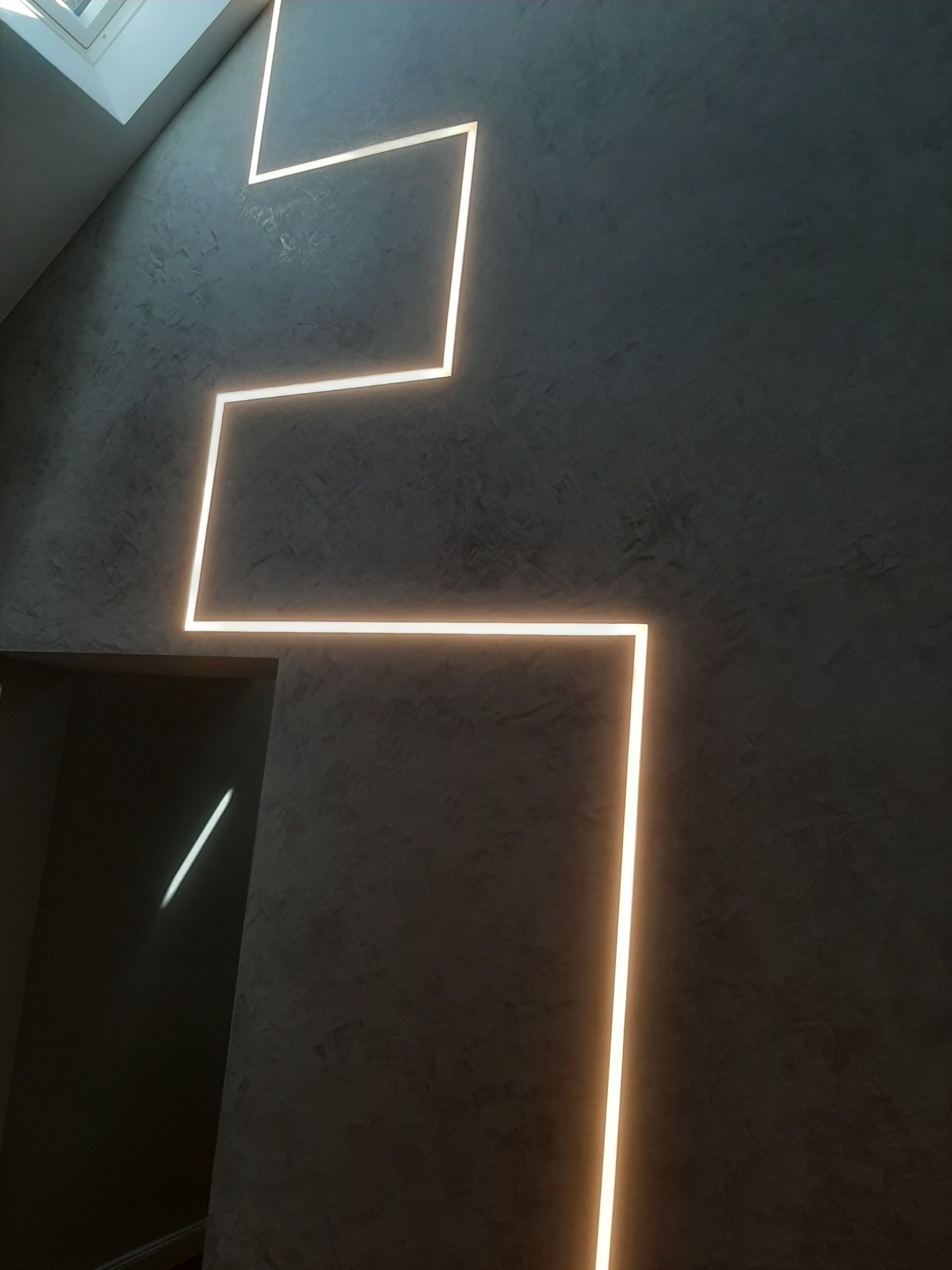 Ściana z szarego betonu architektonicznego z dekoracyjnym oświetleniem LED w kształcie zygzaka, widok z dołu, Rzeszów.