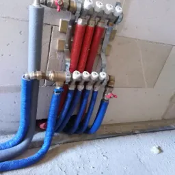 Rozdzielacz instalacji wodnej z rurami w izolacji, czerwonymi i niebieskimi, zamontowany na ścianie z betonu komórkowego.