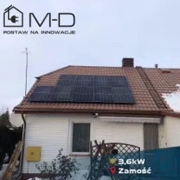 Dom jednorodzinny z brązowym dachem i panelami słonecznymi, widoczny fragment drabiny oparty o rynnę, logo firmy w lewym górnym rogu, informacja o mocy instalacji i lokalizacji w prawym dolnym rogu.