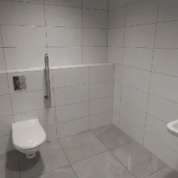 Nowoczesna, minimalistyczna łazienka z białymi płytkami, szarą podłogą, wiszącą toaletą i umywalką, wyposażona w uchwyty dla osób niepełnosprawnych.