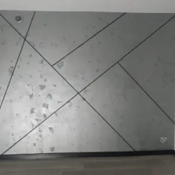 Ściana w salonie z dekoracyjnym szarym tynkiem strukturalnym i czarnymi, geometrycznymi liniami tworzącymi wzór.