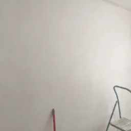 Świeżo zagruntowana ściana w rogu pokoju, widoczne ślady po wałku i drabina malarska z resztkami farby.