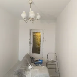 Pokój po świeżym malowaniu na biało, zabezpieczone meble folią, drabina malarska i wisząca lampa w stylu retro.