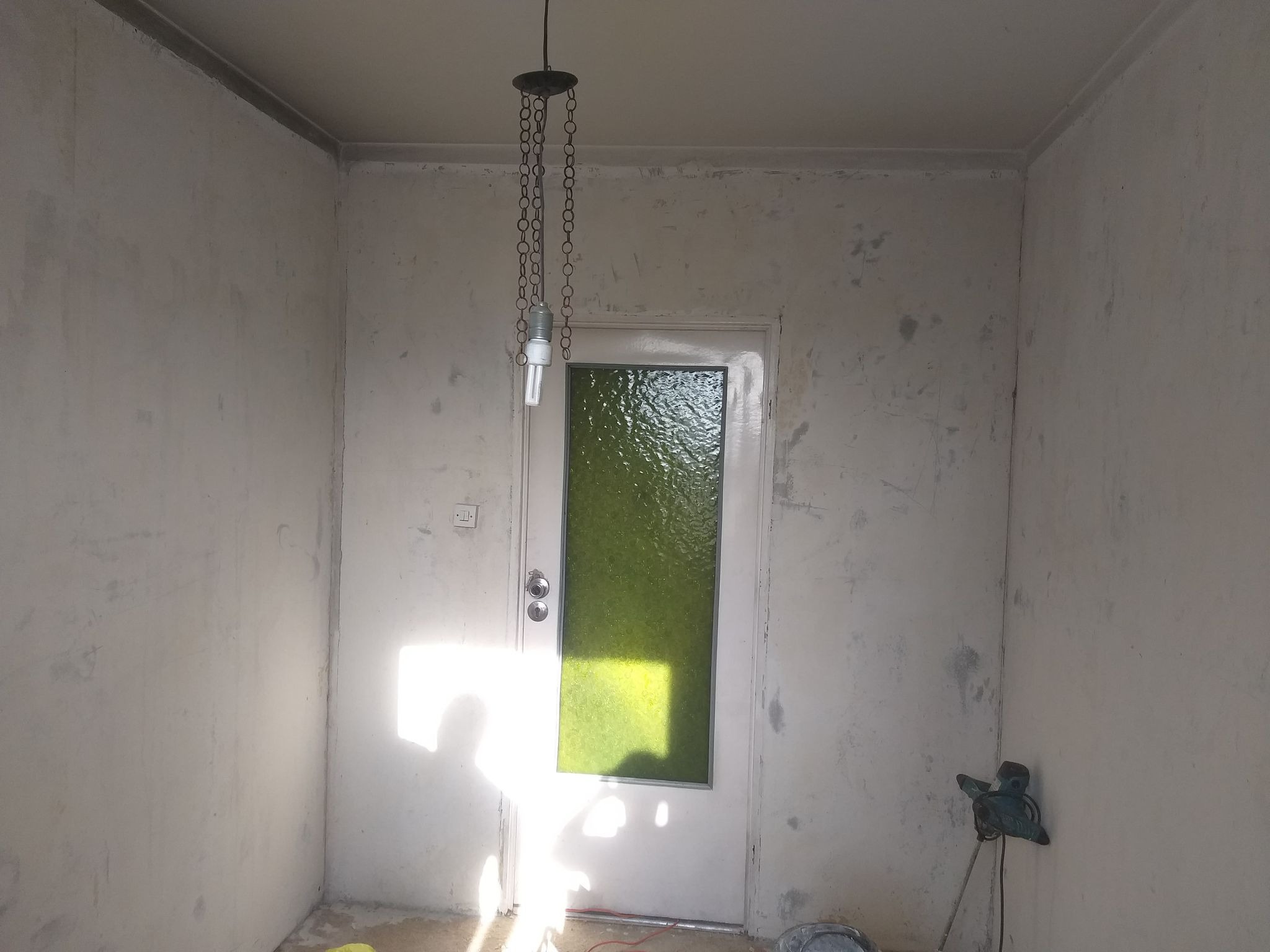 Przygotowane do malowania ściany w pokoju z drzwiami z zieloną szybą, widoczna prowizoryczna lampa na łańcuchu i mieszadło do gładzi w Mysłowicach.