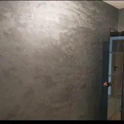 Dekoracyjna ściana w odcieniach szarości z efektem metalicznego połysku, widoczna przy szklanych drzwiach wewnętrznych.