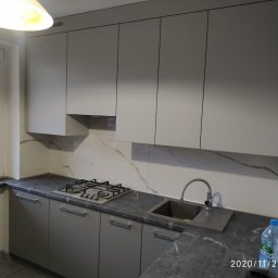 AB Meble Kamyszek Arkadiusz - Nowoczesna kuchnia w odcieniach szarości z marmurowym blatem i backsplashiem, widoczny zlew, płyta gazowa oraz górne szafki bez uchwytów.