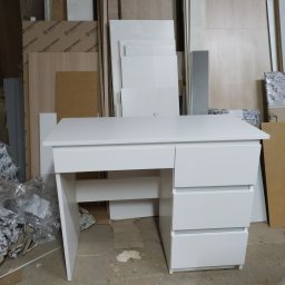 AB Meble Kamyszek Arkadiusz - Białe biurko z szufladami ustawione w warsztacie stolarskim, w tle płyty meblowe Swiss Krono i opakowania folii.