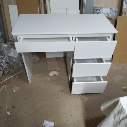 AB Meble Kamyszek Arkadiusz - Białe biurko z szufladami w warsztacie stolarskim, jedna szuflada wysunięta, widoczne płyty meblowe w tle i data na podłodze.