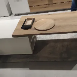 Nowoczesny stolik kawowy z blatem drewnianym i białym modułem z szufladą, na blacie taca i deska do krojenia, w tle meble w podobnej stylistyce.