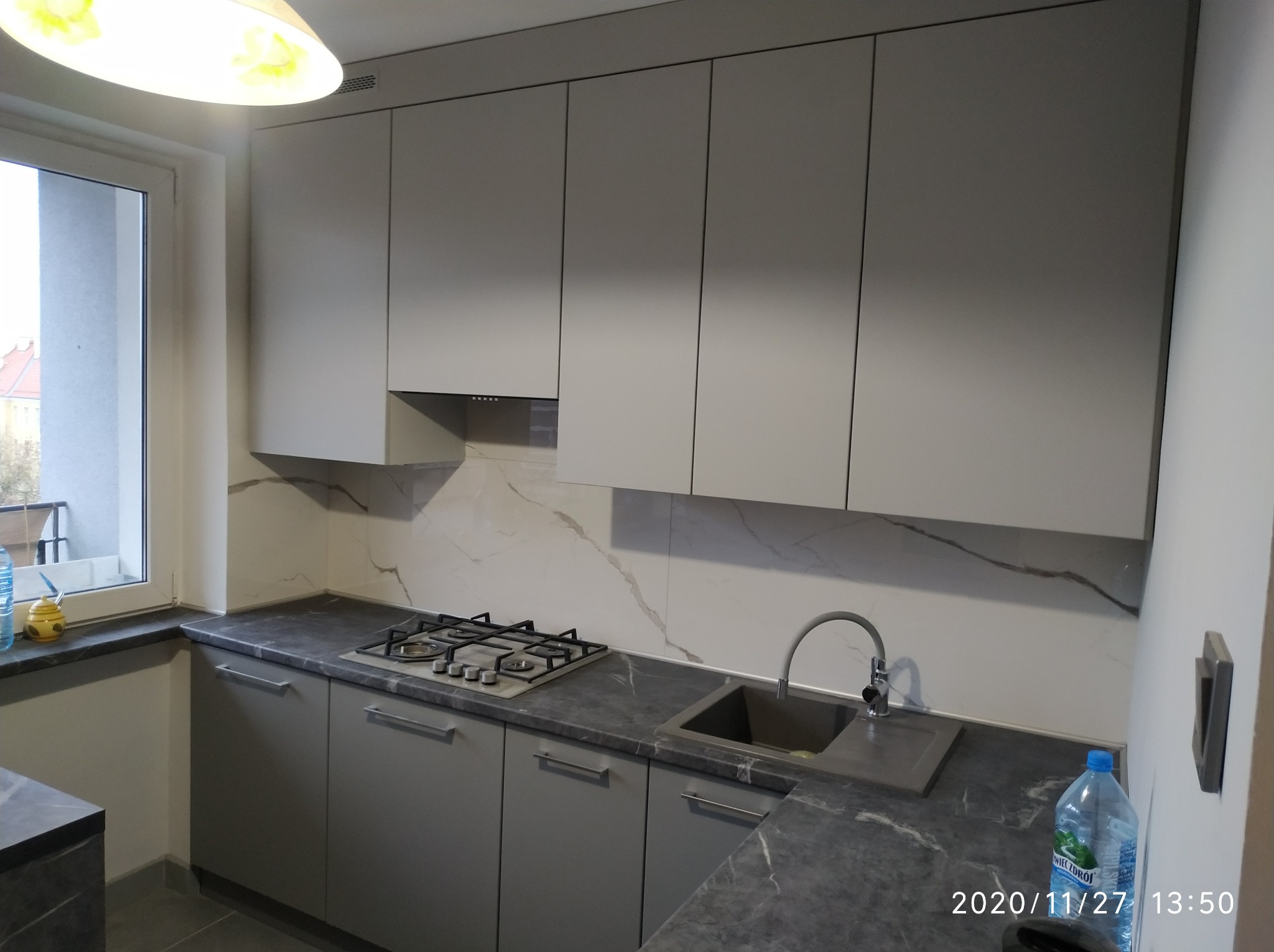 Nowoczesna kuchnia w odcieniach szarości z marmurowym blatem i backsplashiem, widoczny zlew, płyta gazowa oraz górne szafki bez uchwytów.