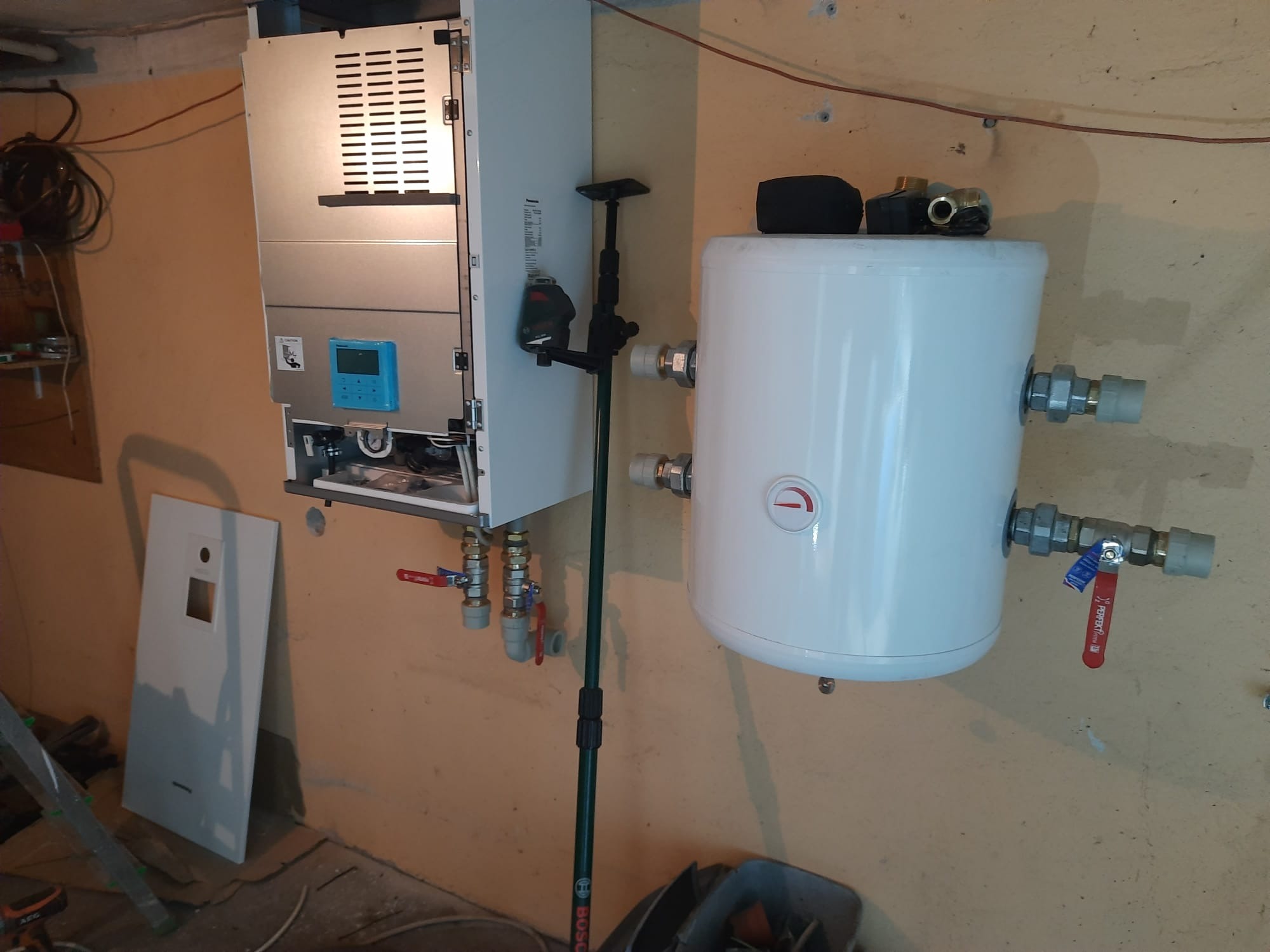 Montaż kotła grzewczego i zasobnika ciepłej wody użytkowej we Wrocławiu, widoczne zawory odcinające na rurach, instalacja w surowym stanie.