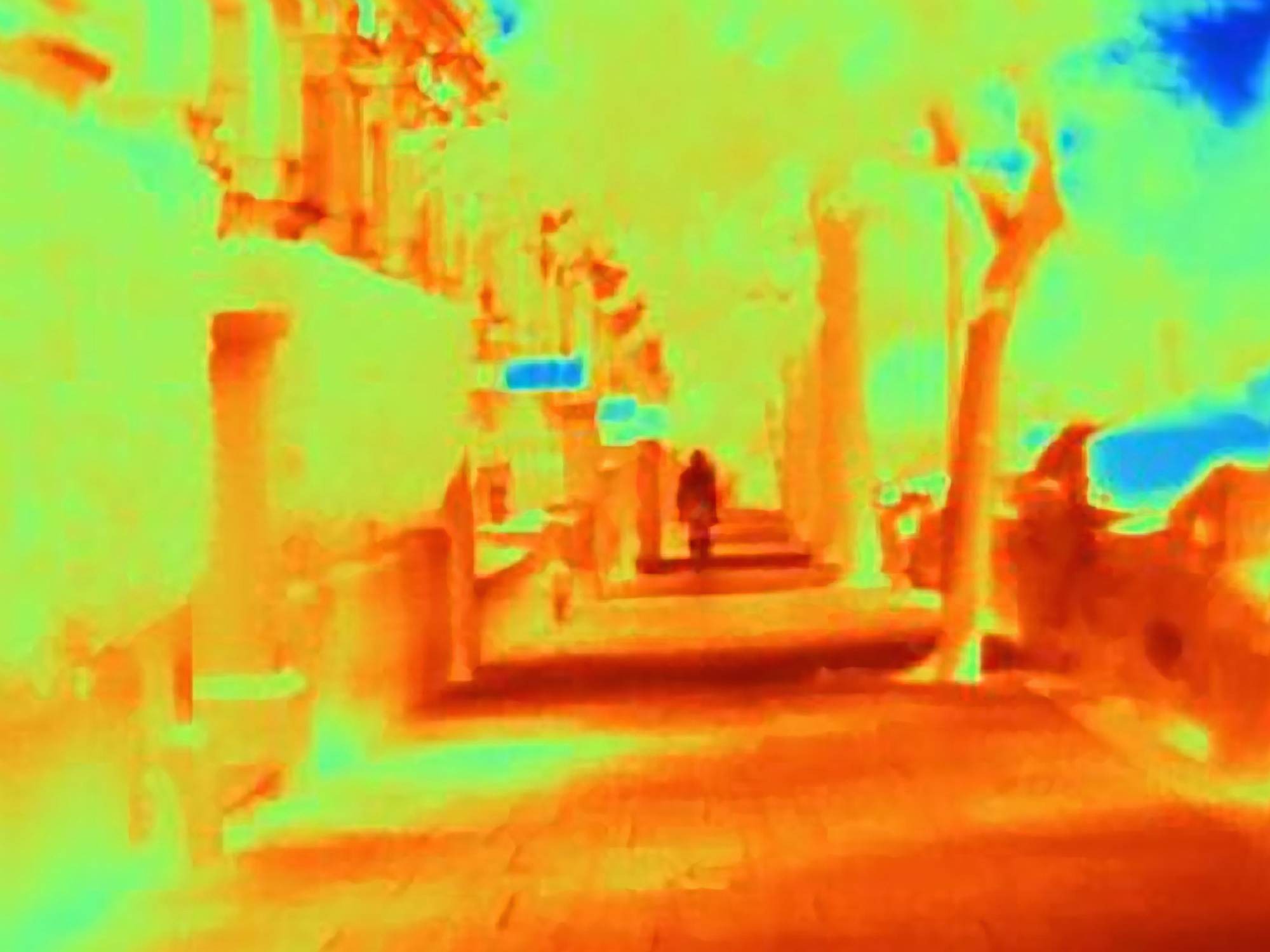 Termowizja elewacji budynku z widocznymi mostkami termicznymi i stratami ciepła, zarys postaci na chodniku.