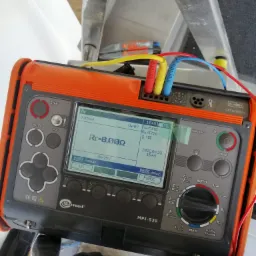 Pomiar rezystancji uziomu za pomocą miernika Sonel MPI-520 z podłączonymi przewodami pomiarowymi w kolorach niebieskim, czerwonym i żółtym, wyświetlacz pokazuje wynik pomiaru 8,000 omów, urządzenie...